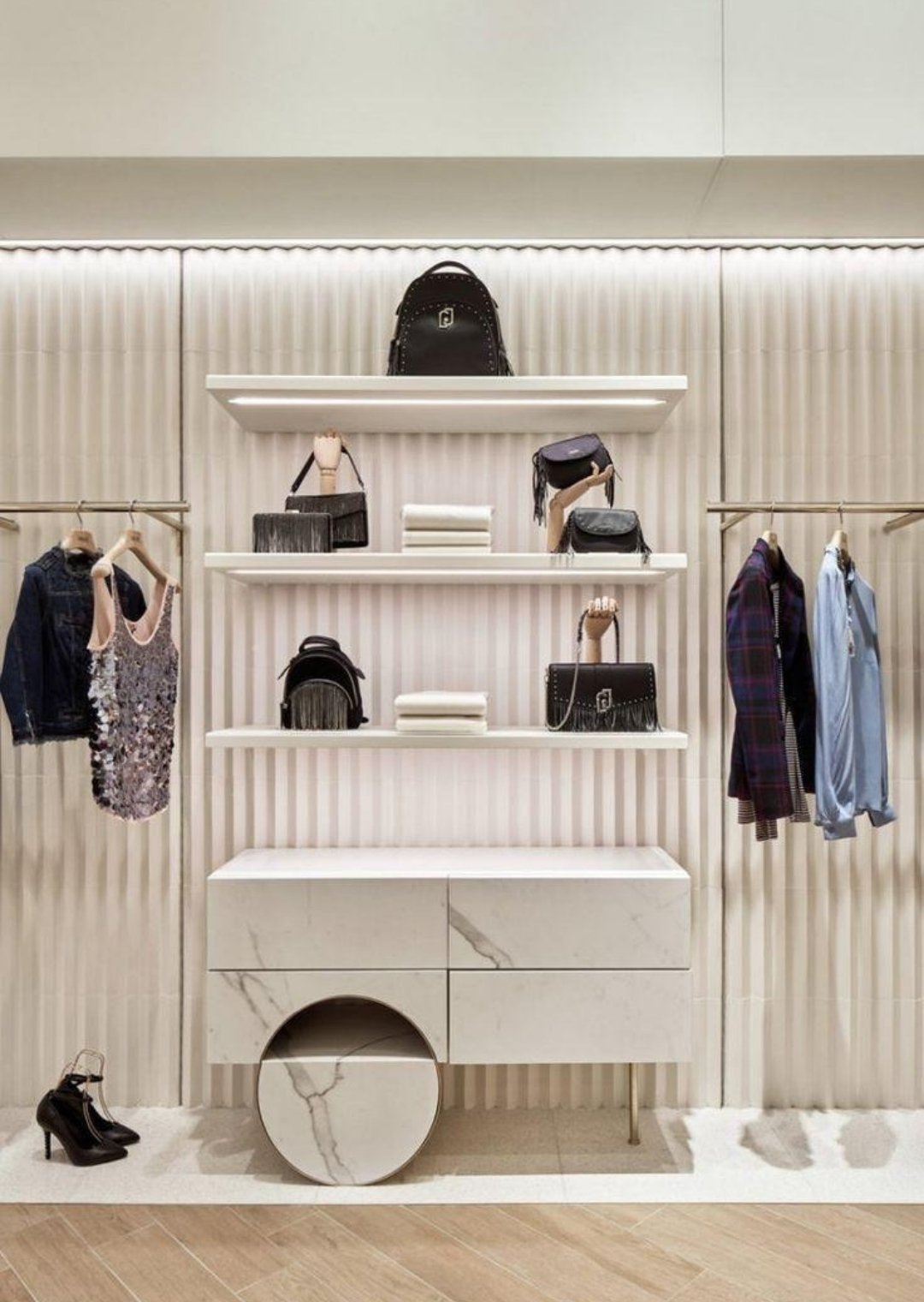 Minimal ράφια και display καταστήματος με τσάντες, διπλωμένα ρούχα και φωτισμό για κομψή και οργανωμένη εμπορική παρουσίαση.