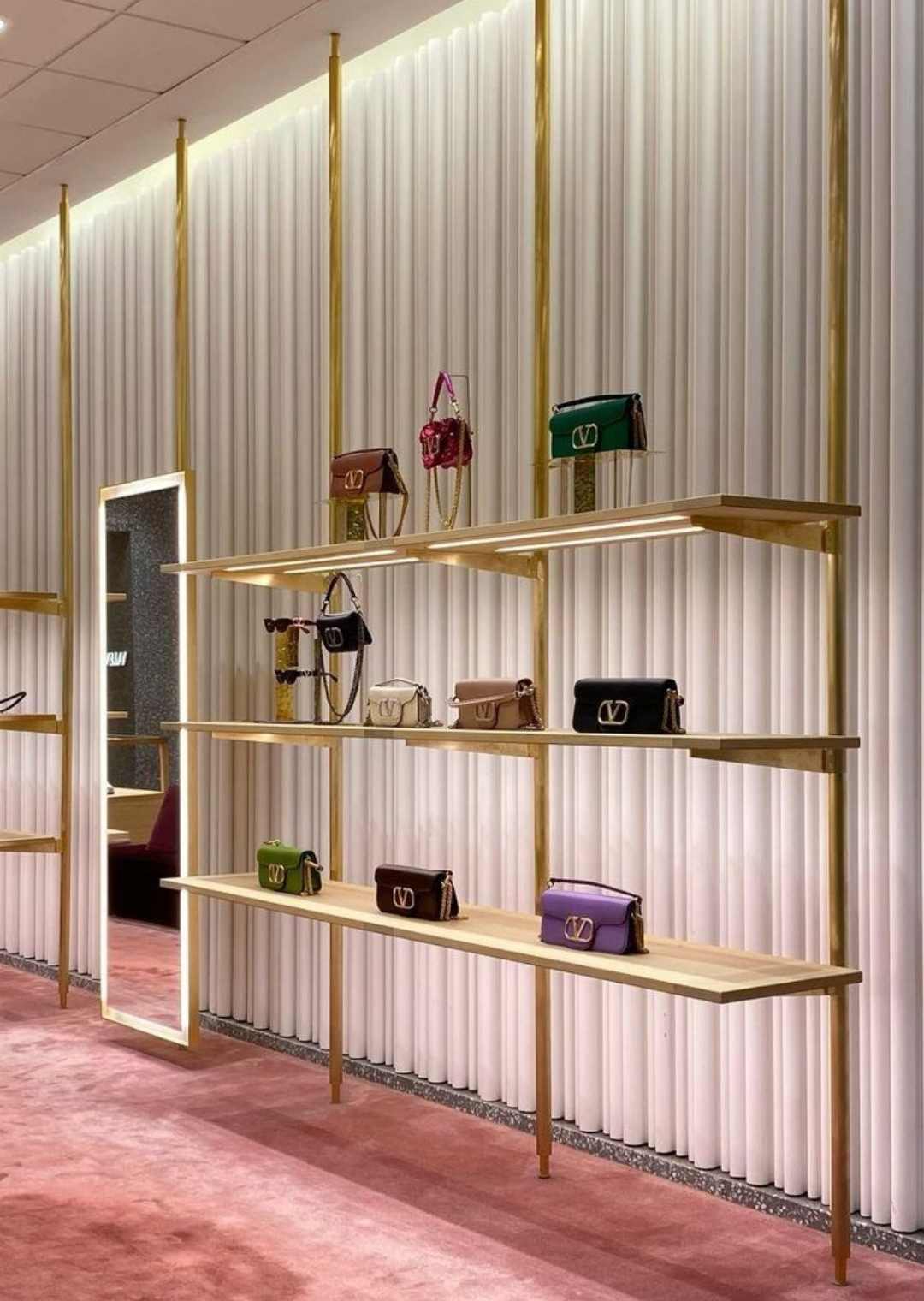 Χρυσά ράφια καταστήματος με γυναικείες τσάντες και ατμοσφαιρικό φωτισμό που αναδεικνύει την premium παρουσίαση προϊόντων.